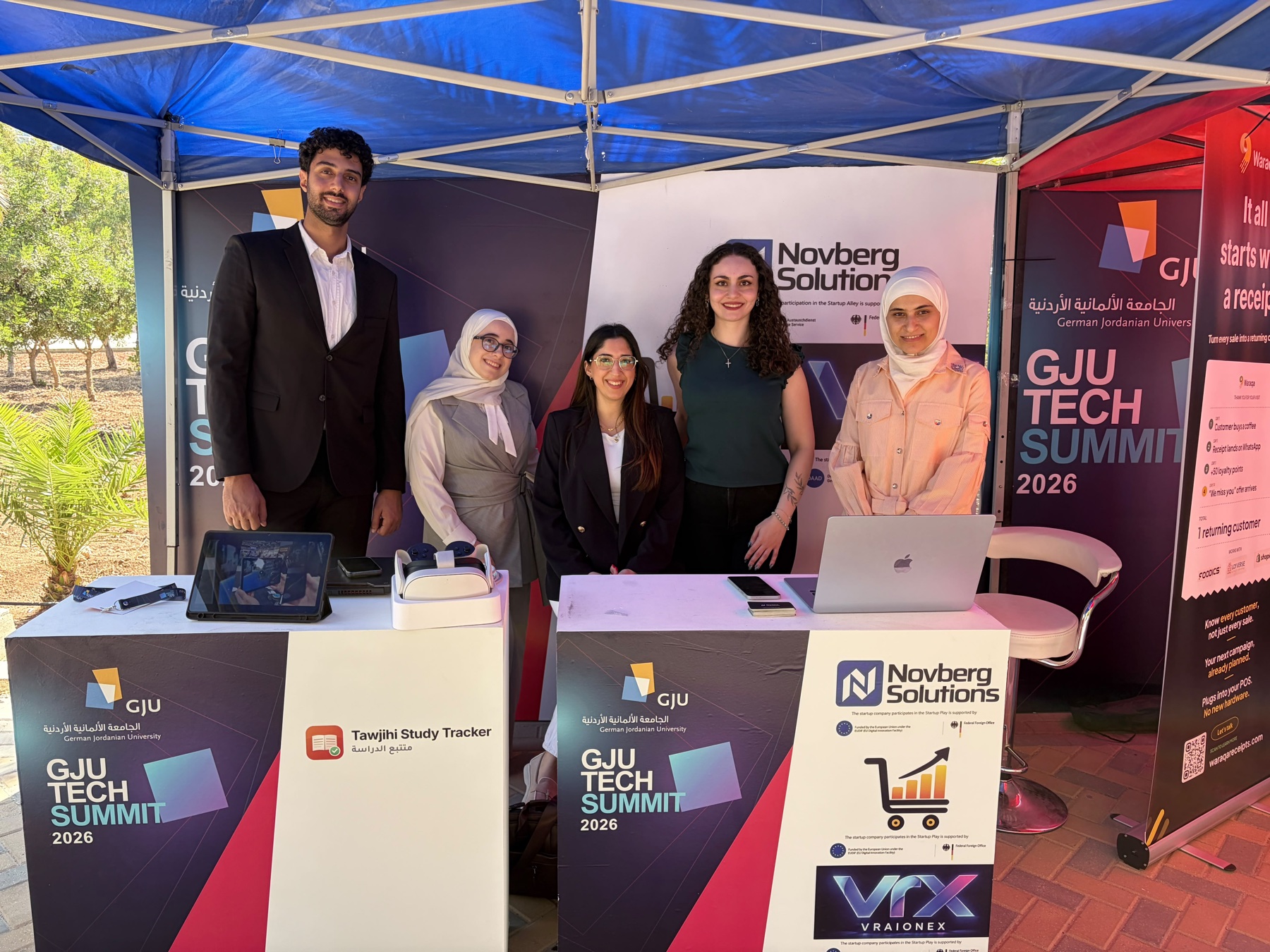 Five participants at exhibition stands displaying Syrian startup branding at GJU Startup Alley 2026.